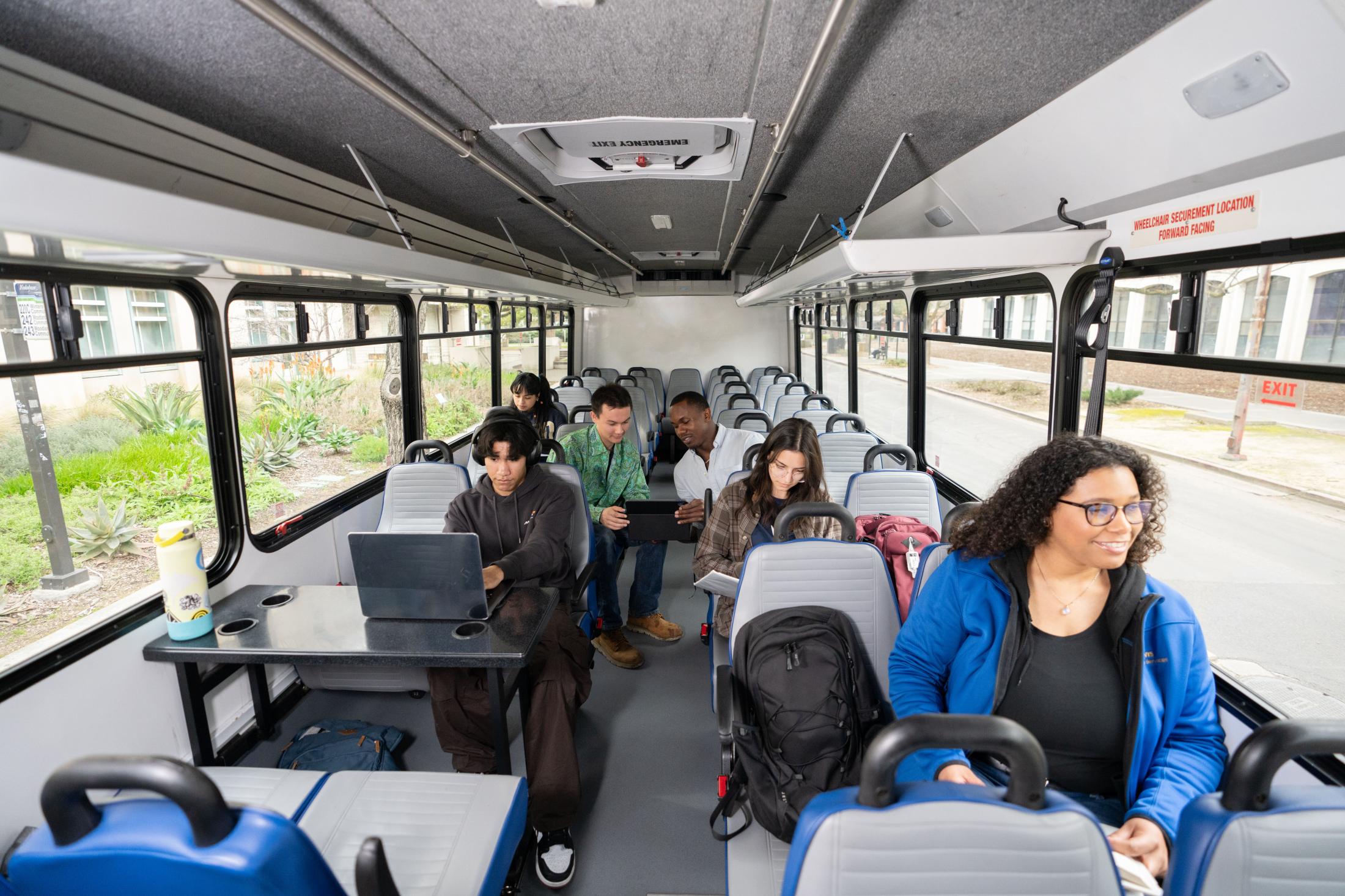 Students smiling and using electronic devices while aboard the shuttle.