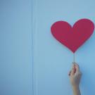 blue paper heart being held by a person standing next to a blue painted wall